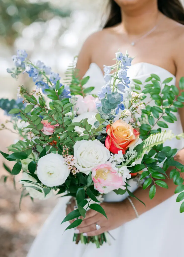 Bride holding a colorful garden bouquet of blue, pink and orange blooms